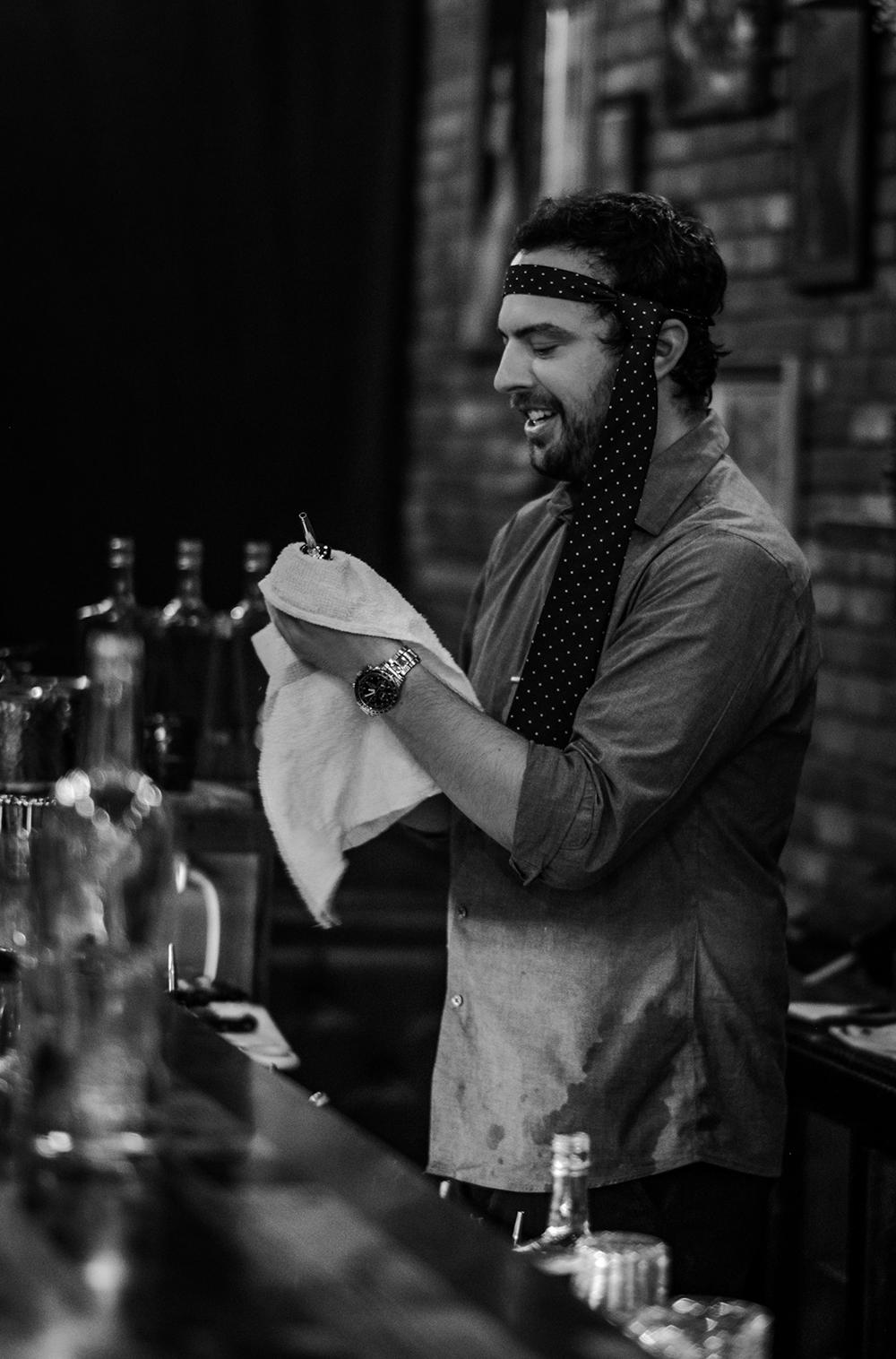 Jordan Black, founder of the Hunderberg Club, polishing barware while wearing a polka-dot tie as a headband